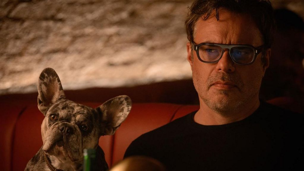 Jemaine Clement as Steve sitting on a sofa with a dog next to him 