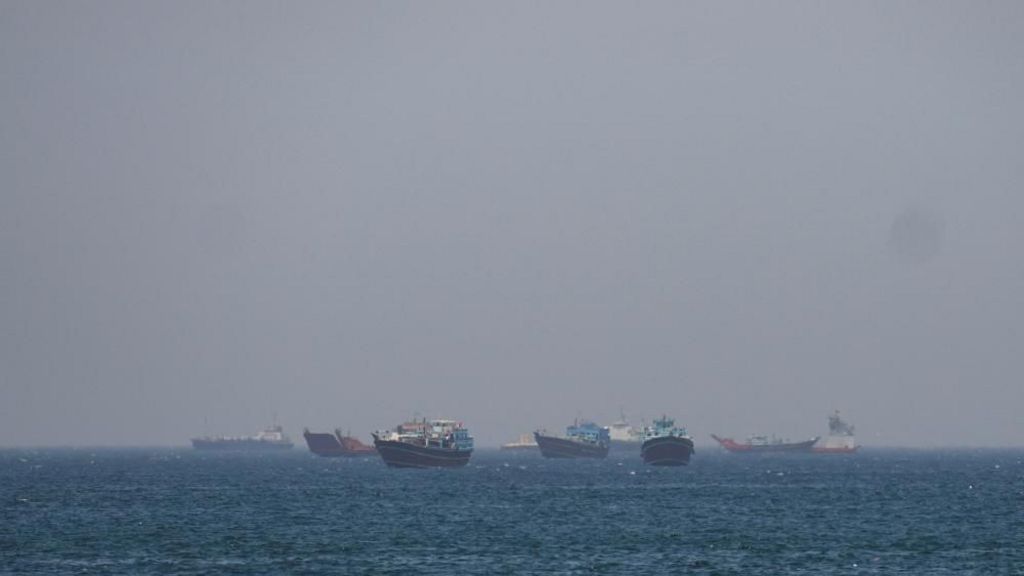 Large boats sitting about in the water close to one another. It's a hazy day and the boats on the horizon are harder to make out due to the haze 