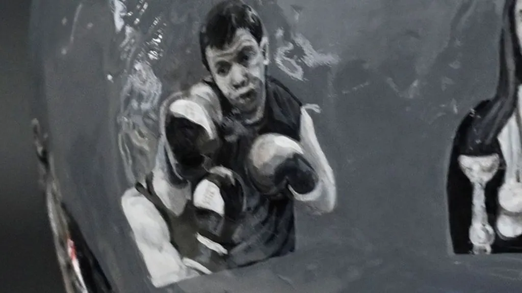A close up shot of the helmet featuring a black and white illustration of Maksym Halinichev. He is wearing boxing gloves and is sparring.