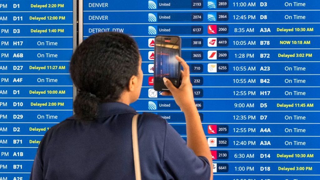  A woman uses the camera on her phone to record a flight information board showing multiple delays and some cancellations in flight departures from Dulles International Airport on July 19, 2024 in Dulles, Virginia.