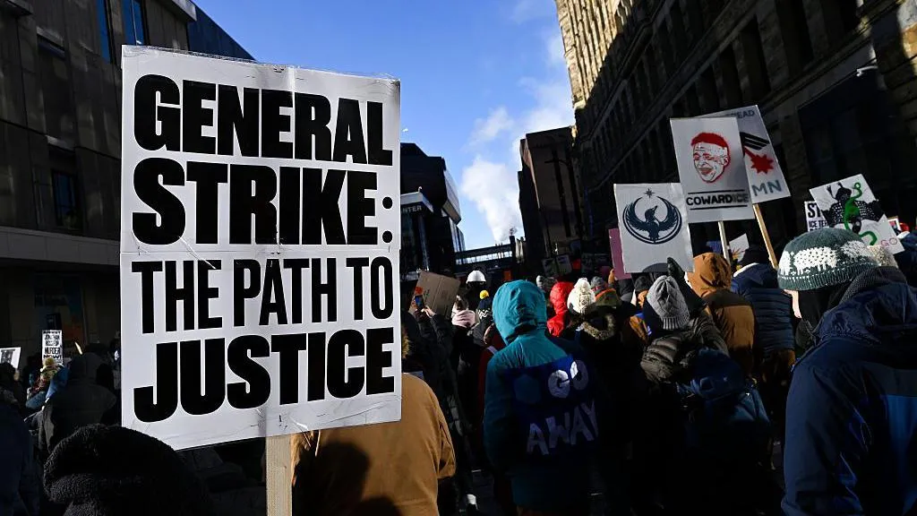 A protester with a sign saying 'General Strike: The Path to Justice' amid a larger crowd