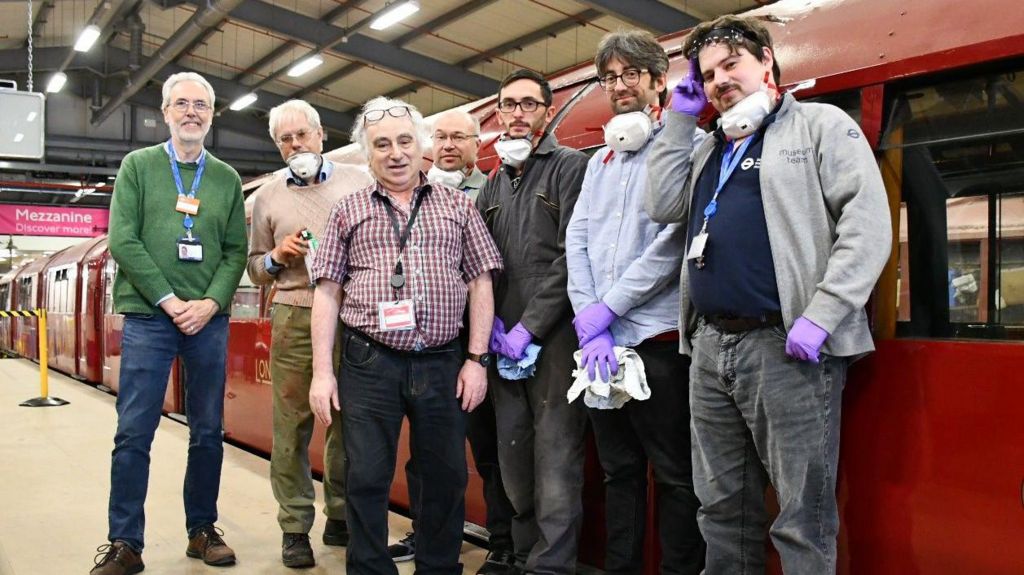 Seven men, three of who are wearing purple gloves, standing by the restored train