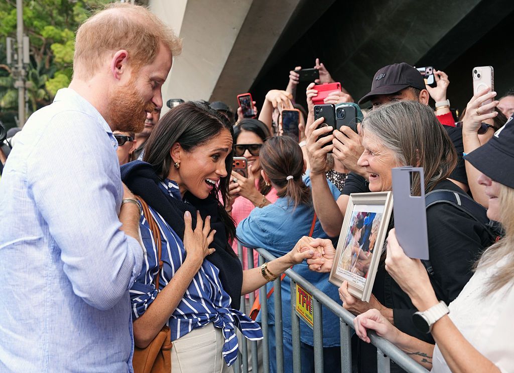 Harry and Meghan react emotionally to a fan showing them a framed picture.