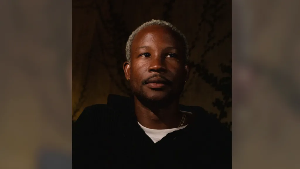 A man in a black hoodie with bleached blonde hair looks to the right of the camera