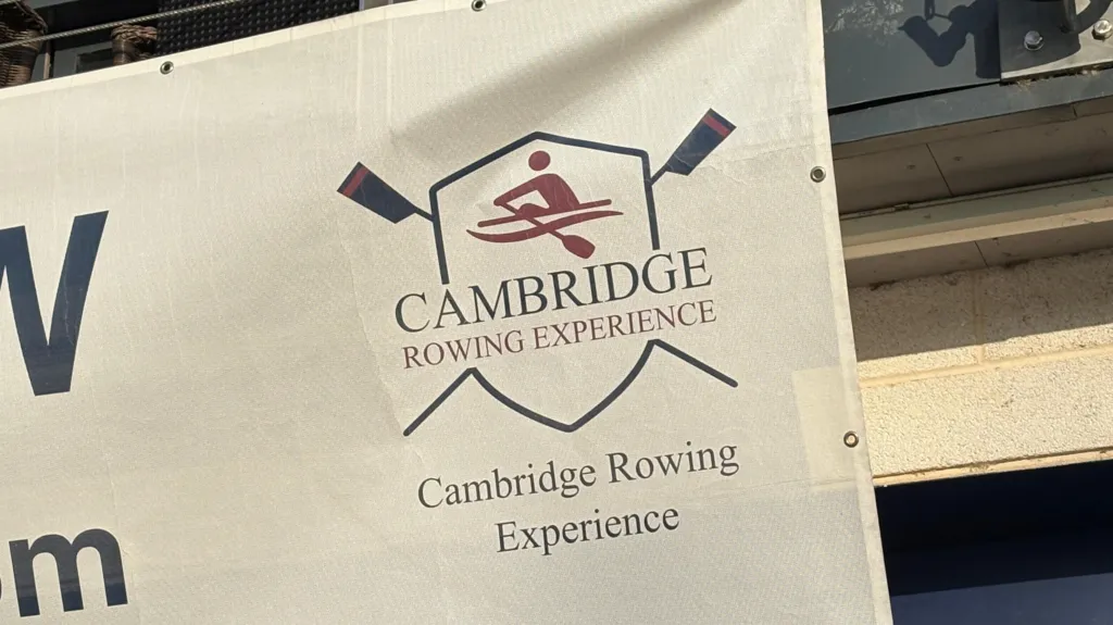 The corner of a white banner, which is hung on the outside of a rowing club's boathouse. This part of the banner shows a logo with the words 