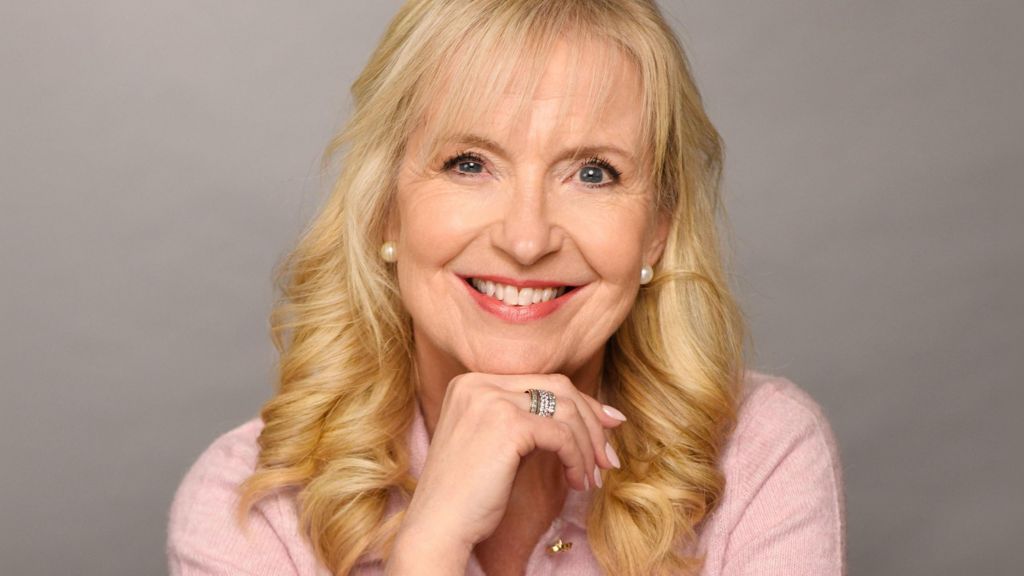 Carol Kirkwood smiling and resting her chin on her hand while wearing a pink top