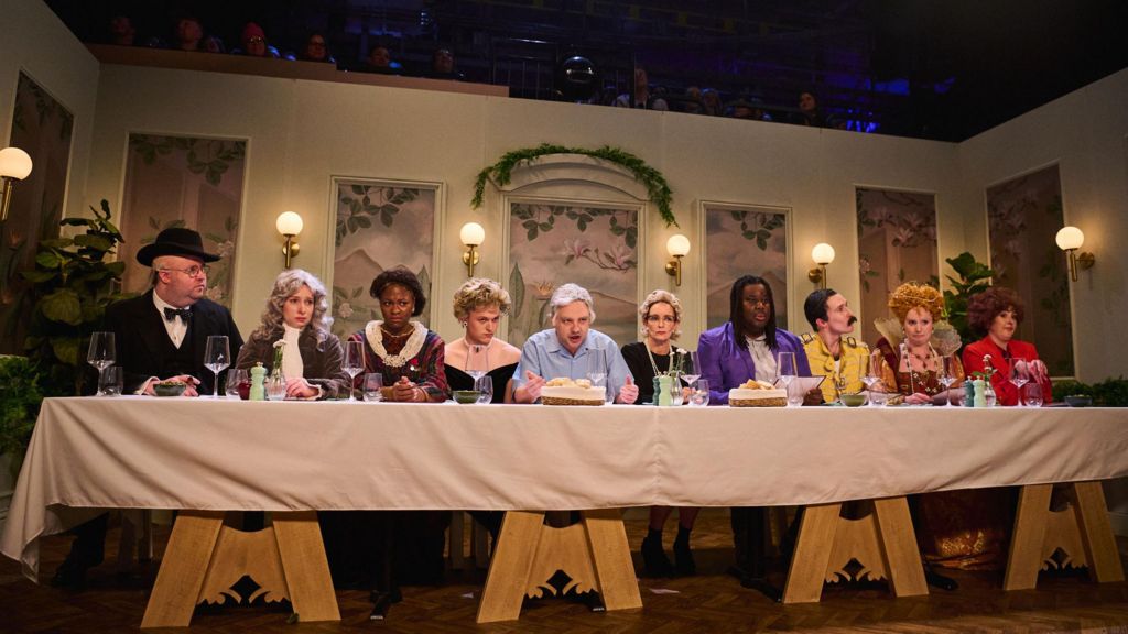 Cast members of Saturday Night Live UK sit at a long table resembling the Last Supper, with an actor playing David Attenborough in the middle, and others including Freddie Mercury and Winston Churchill alongside him