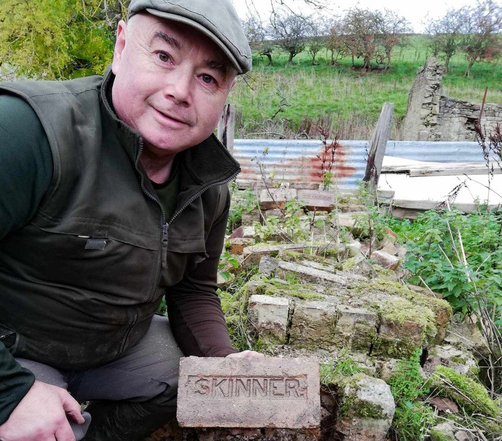 Chris Tilney holding a brick at a derelict farm
