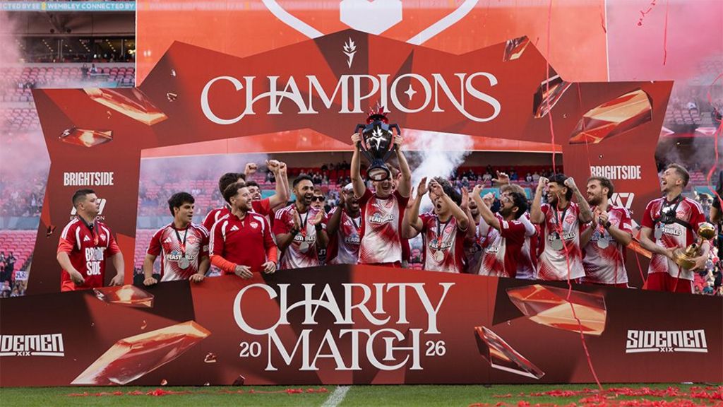 A trophy celebration for the YouTube Allstars, with red boards with white writing reading "Champions" and "Charity match", as players celebrate.