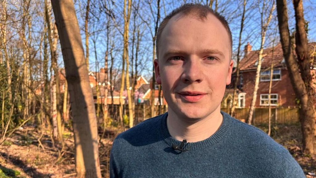 First-time buyer Henry pictured outside among some trees and wearing a blue jumper