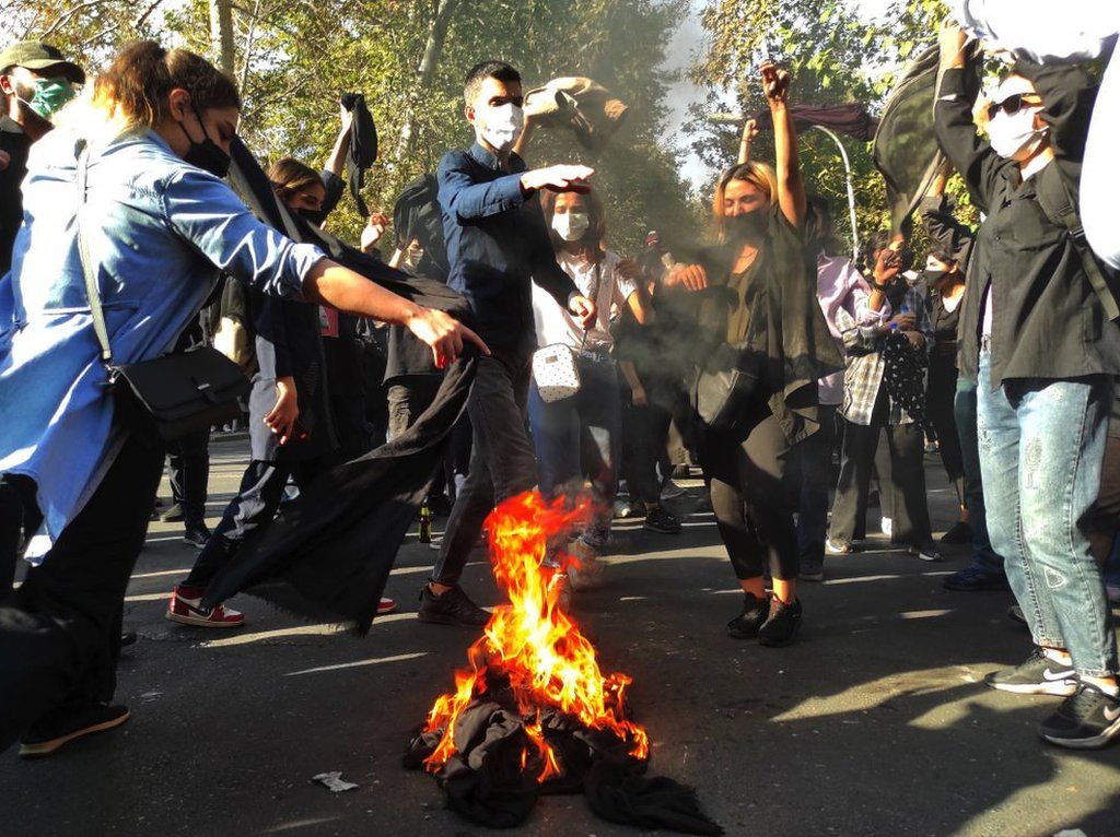 Iranian protesters set their scarves on fire while marching down a street on 1 October 2022 in Tehran