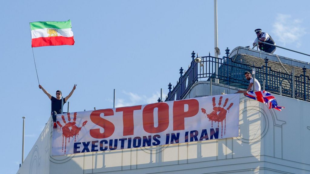 Protesters hold a banner saying "stop executions in Iran" and wave an Iranian flag during a demonstration on the roof of the Trocadero, overlooking Piccadilly Circus, central London (30 July 2026)