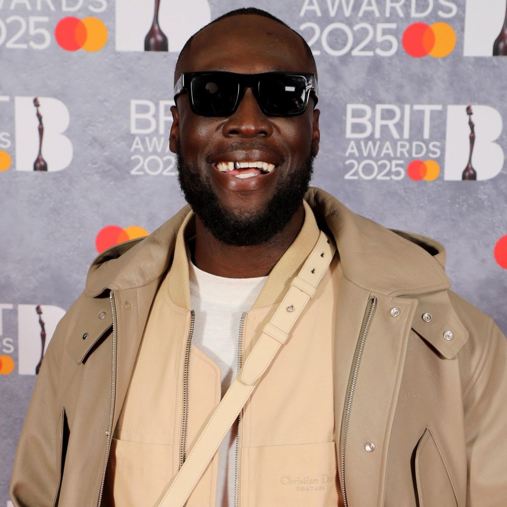 Stormzy smiles for the camera while wearing sunglasses, as he poses on the Brit Awards red carpet.