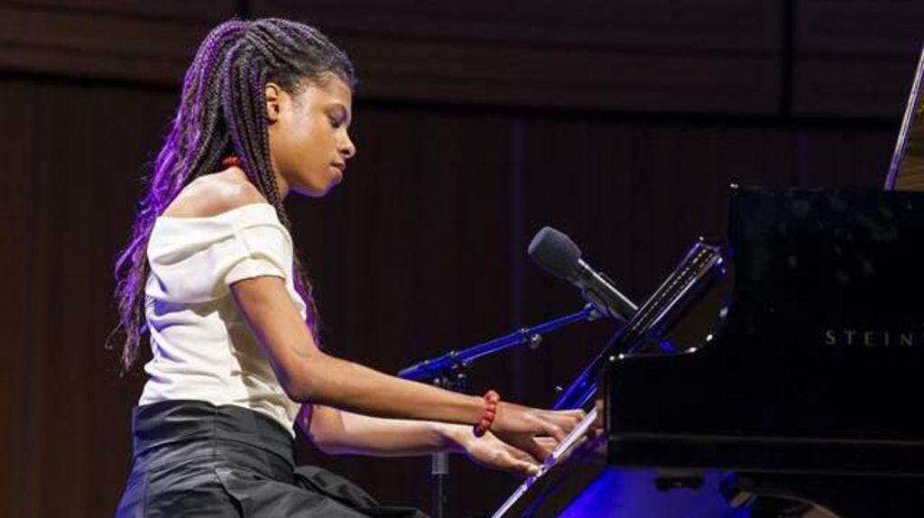 Mia Odeleye, a teenage girl, playing a piano on a stage