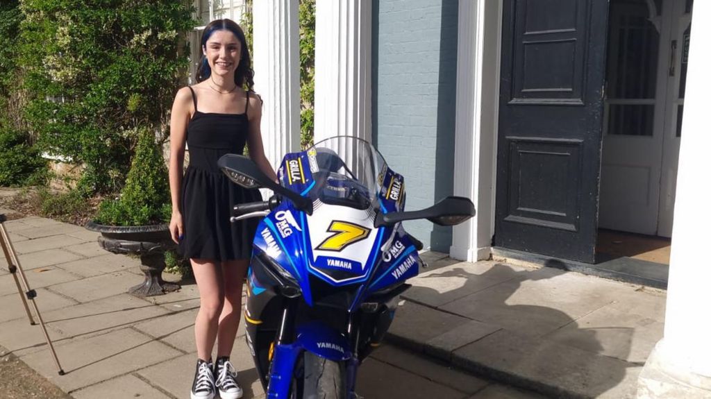 Scarlett Alexander in a black dress standing in front of Caistor Hall Hotel with a blue OMG replica superbike