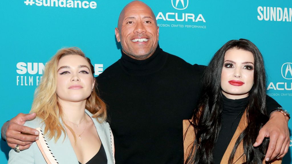 Florence Pugh, Dwayne Johnson, and Suraya Knight aka Paige attend the surprise screening of Fighting With My Family during the 2019 Sundance Film in Utah. Pugh is wearing a powder blue jacket, Johnson is dressed in a black polo neck, while Paige has a tanned jacket on.