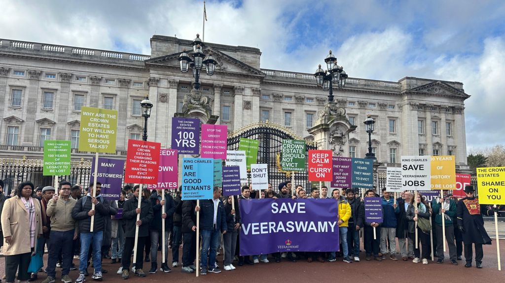 A large group of protesters outside Buckingham Palace, with multiple coloured placards saying "keep calm and curry on", "many customers are heartbroken", "stop the greedy crown estates from evicting Veeraswamy".