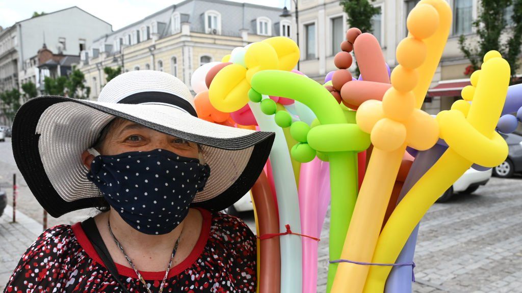 A woman in a face mask selling balloon swords smiles at the camera in Tbilisi, Georgia