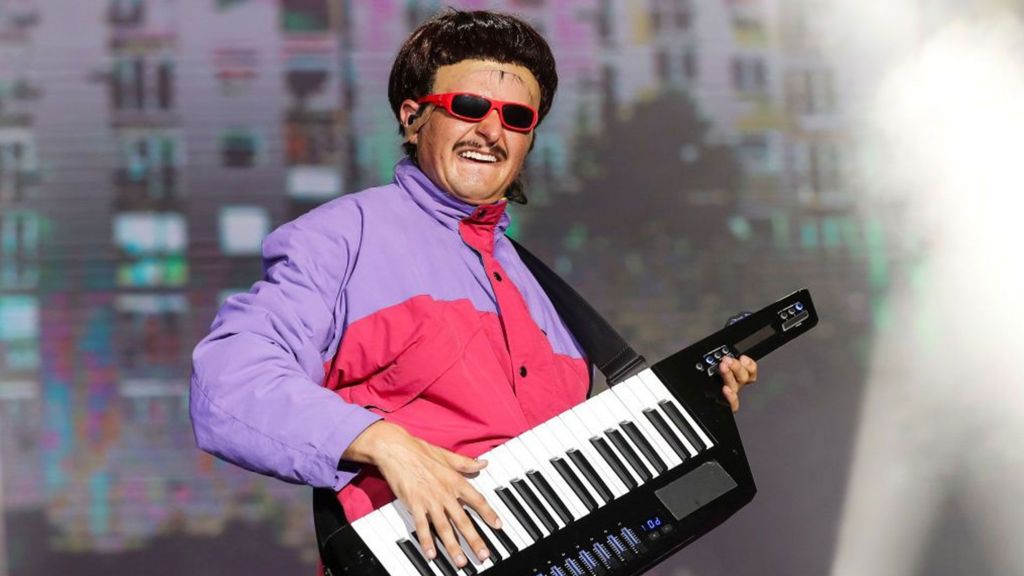 Picture of Oliver Tree in a purple and pink jacket performing in 2024. He is holding a keyboard.