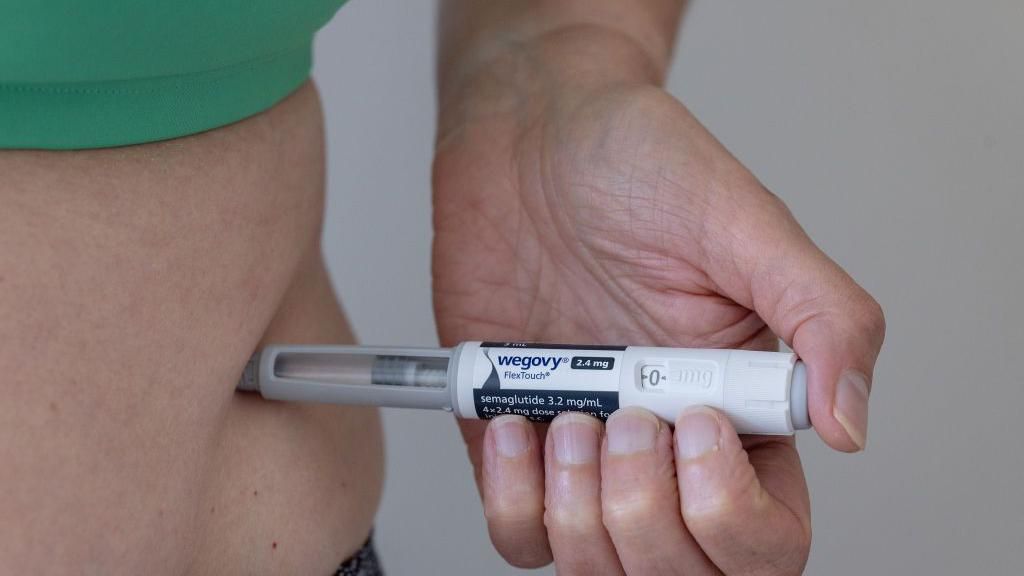 A person wearing a green top injects Wegovy into their stomach. 