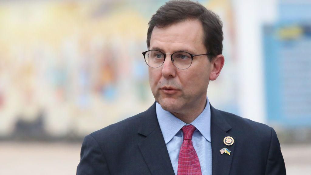 Tom Kean Jr in wire framed glasses, a blue suit and pale blue shirt, with a red tie.
