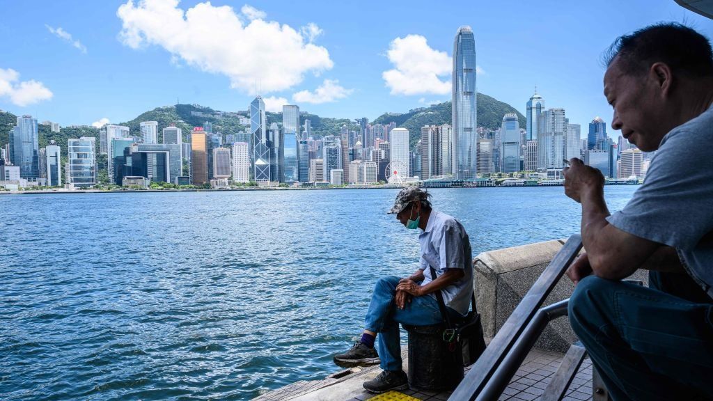 A man sits along the Kowloon side of Victoria Harbour which faces the skyline of Hong Kong Island.