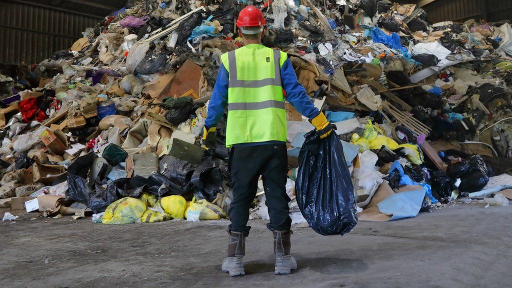 man standing in front of mountain of rubbish