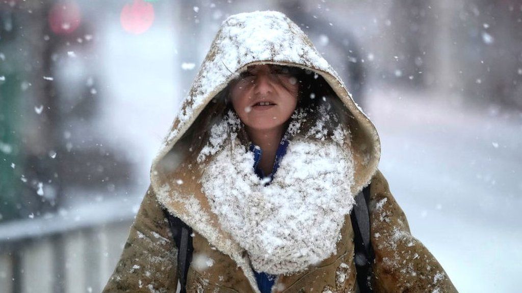 A woman covered in snow walks down the street