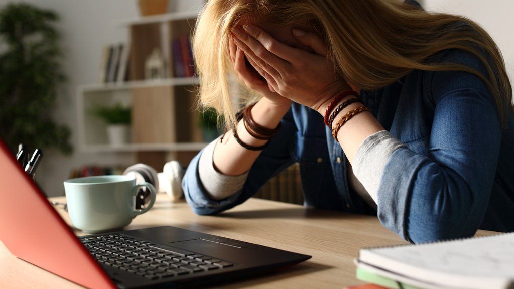 Stock image of a sad woman head in hands in front of a laptop