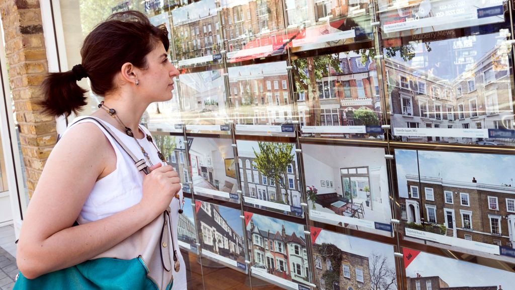 A woman looking in an estate agent window at houses being advertised