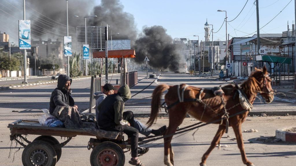 Horse drawn cart moves past smoke near Salah al-Din Road as Israeli attacks continue in central Gaza