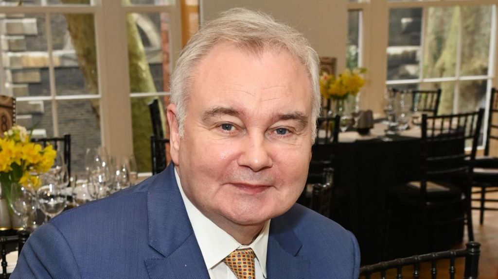 A headshot from 2024 of Eamonn Holmes wearing a blue suit and yellow tie