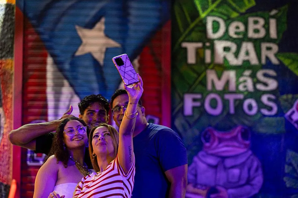 A group of people take a selfie in front of a colourful mural