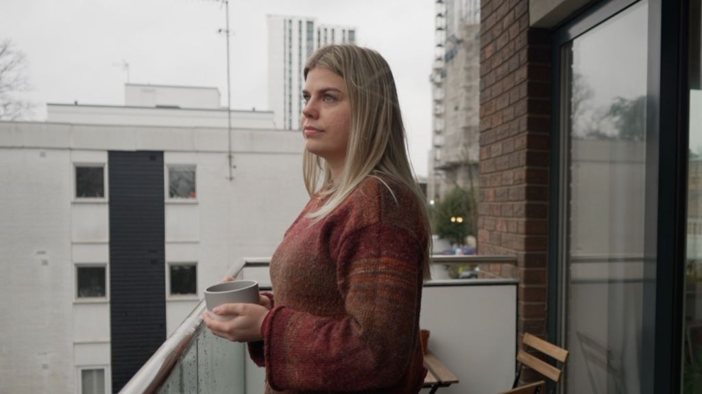 Deryn Harris is standing on her balcony holding a grey mug and looking out over the city
