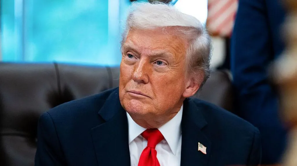 US President Donald Trump pictured in the Oval Office of the White House. The close-up shot shows him, dressed in a navy blue suit and a red tie, looking to his right