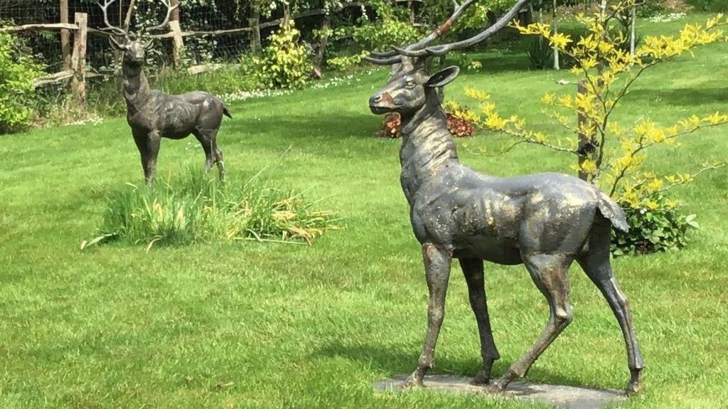 Two black and gold stag statues placed on green grass.