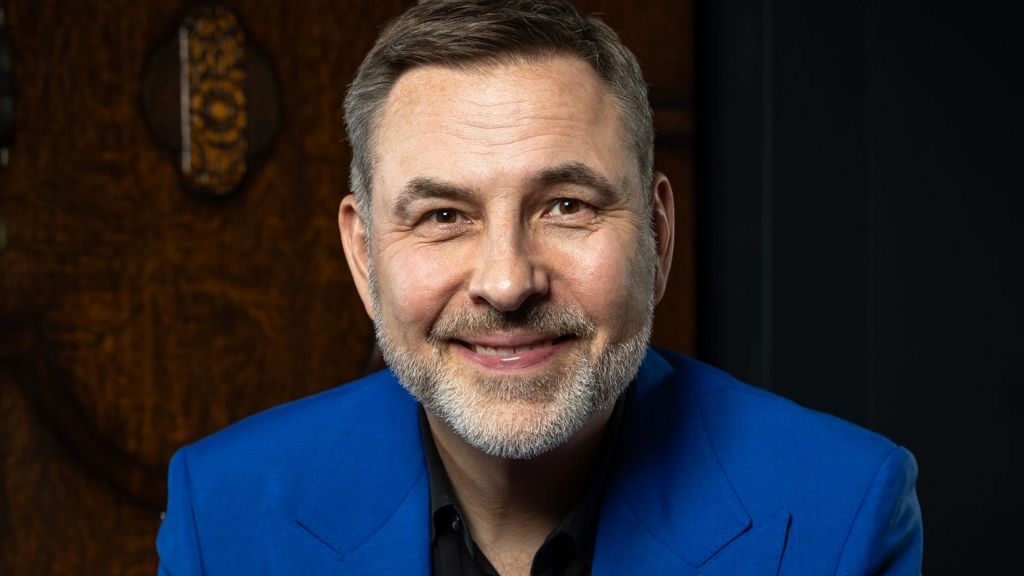 A close up photo of David Walliams in a bright blue suit smiling at the camera 
