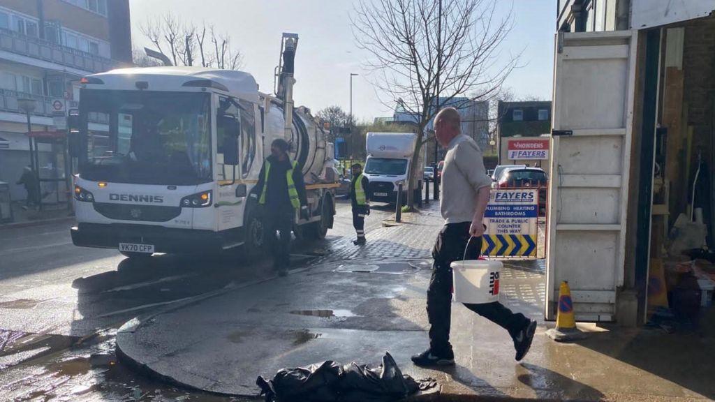 A warehouse with an open door. A man is walking out of it holding a bucket.