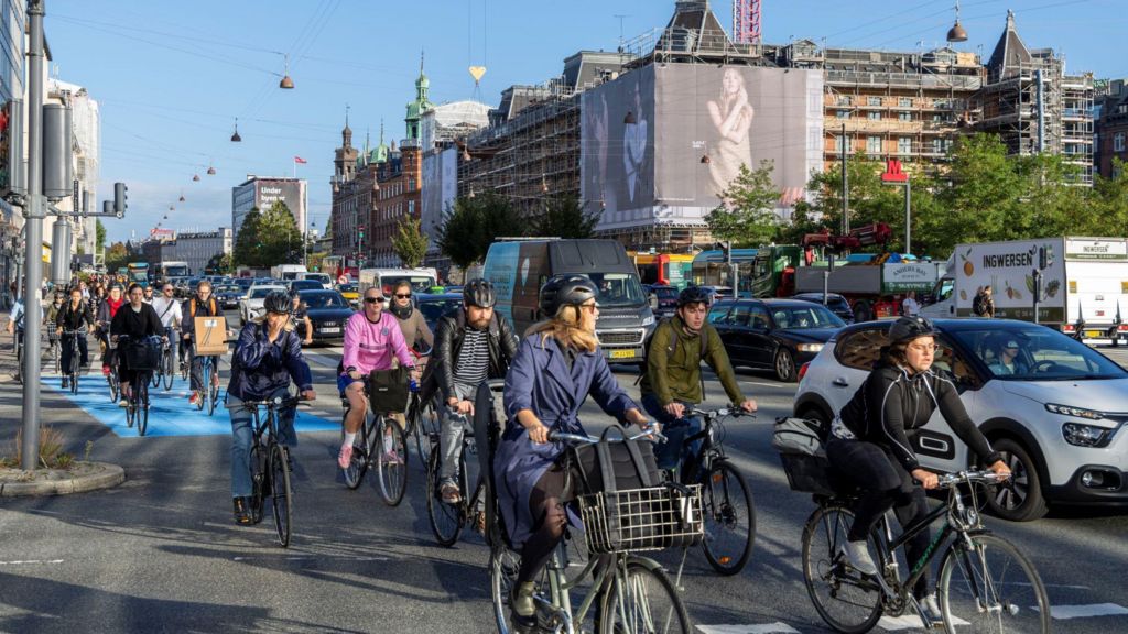 Lots of men and women riding bikes next to a road in a city