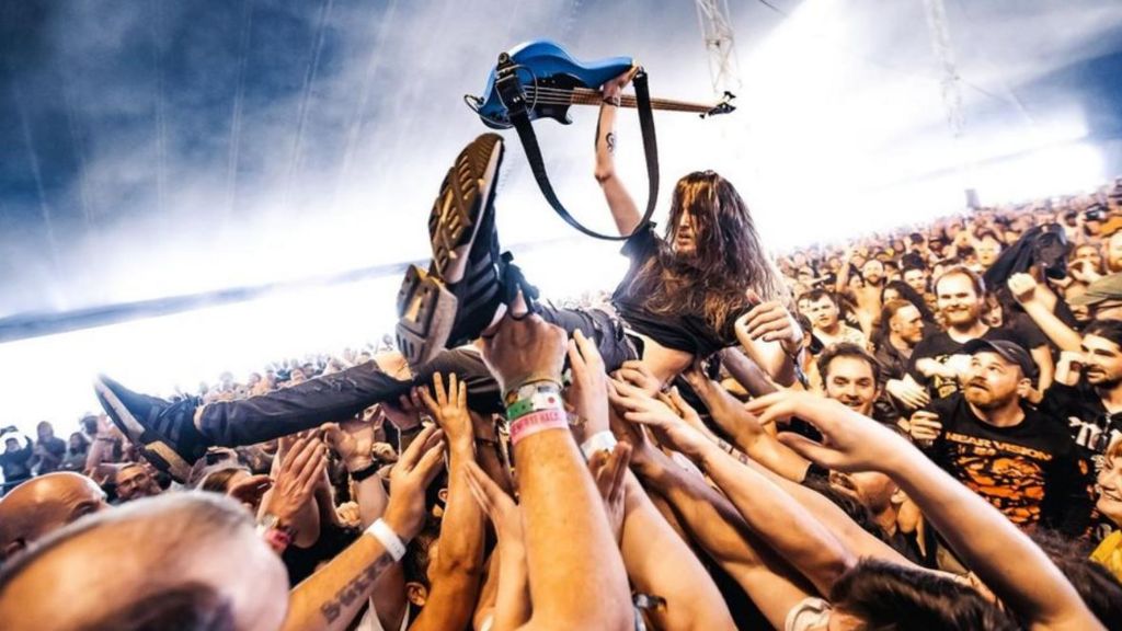 A man crowdsurfing while holding up his guitar