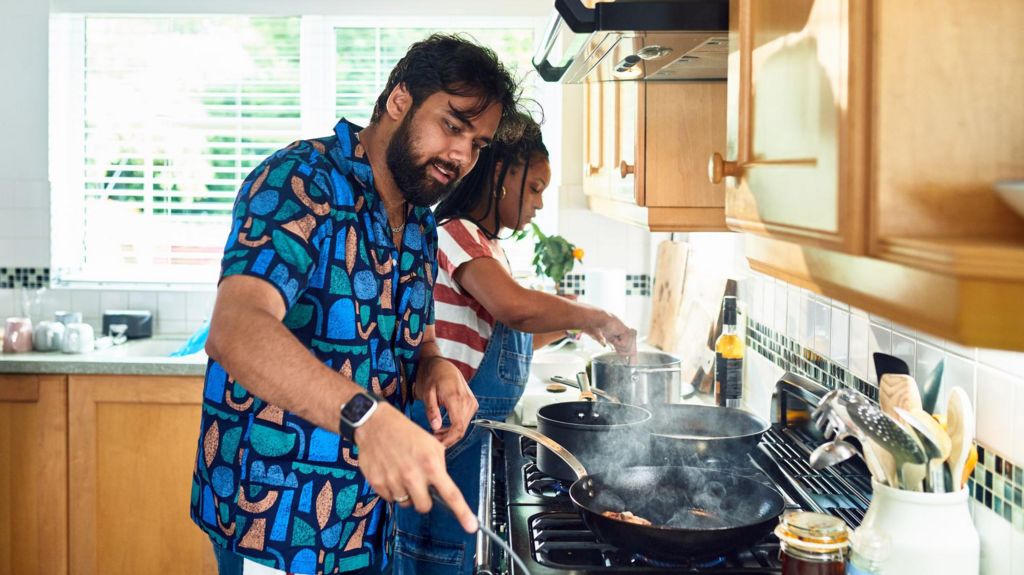 Couple cook on a hob in a kitchen.