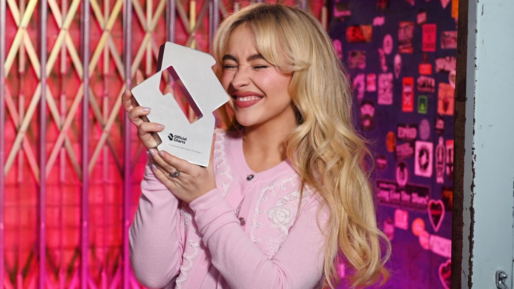 Sabrina Carpenter holding up her number one trophy from the Official Charts Company