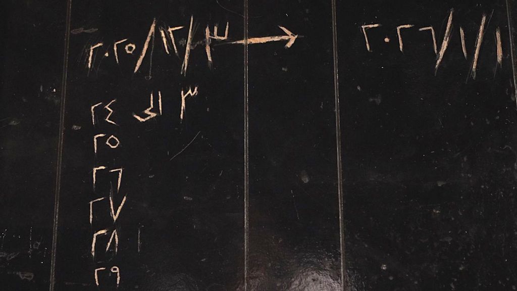 Black-painted wall with dates in Arabic scratched into it