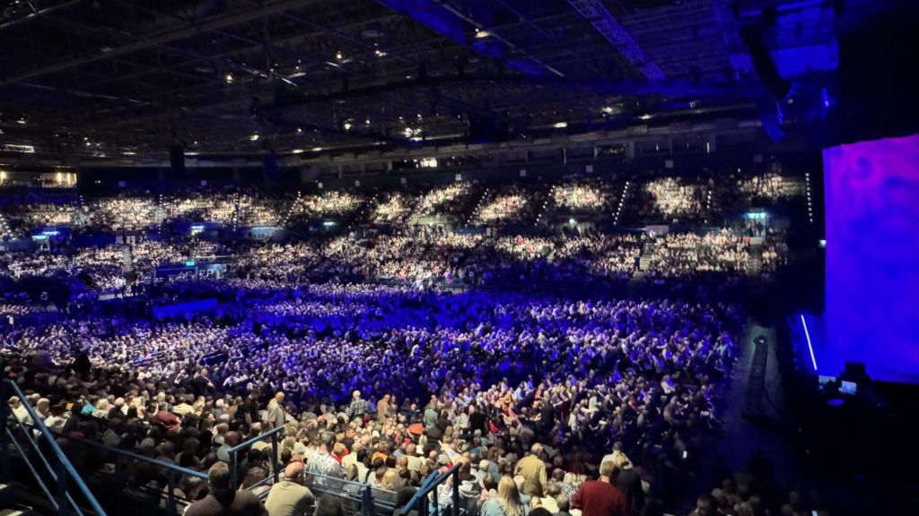 A wide photo of an indoor arena with many people inside.