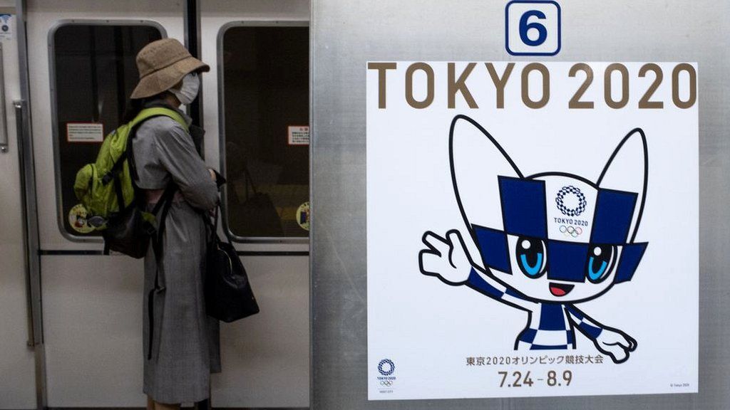 A passenger wearing a face mask stands next to a poster of Tokyo 2020 Olympic mascot Miraitowa on a train in Tokyo on April 20, 2020