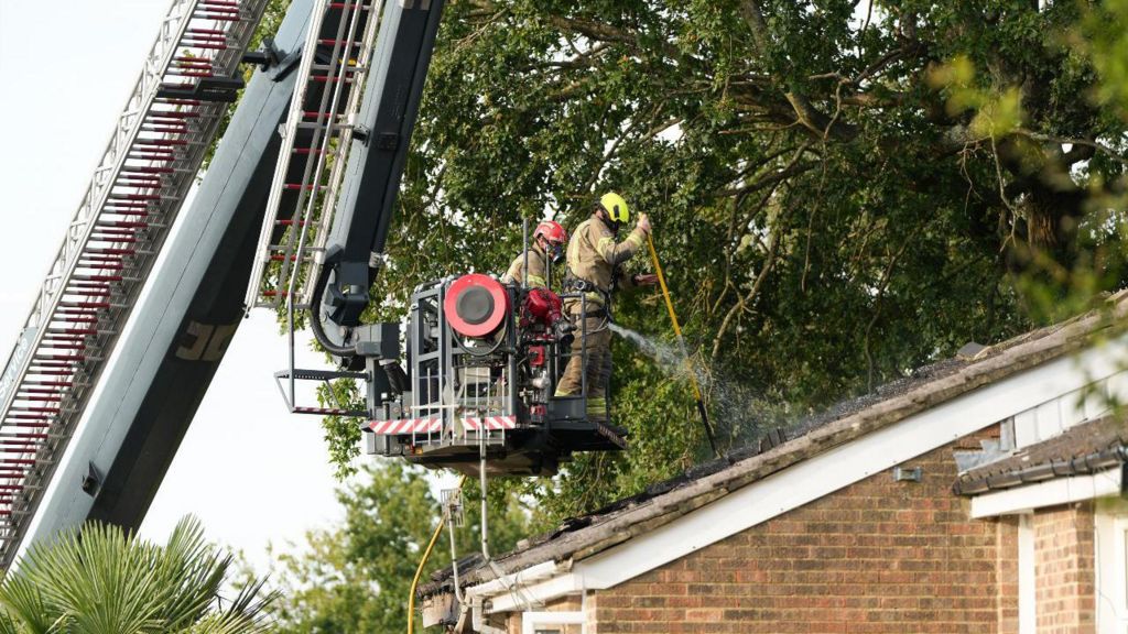 Two firefighters on a crane spray a roof of a house with water. 