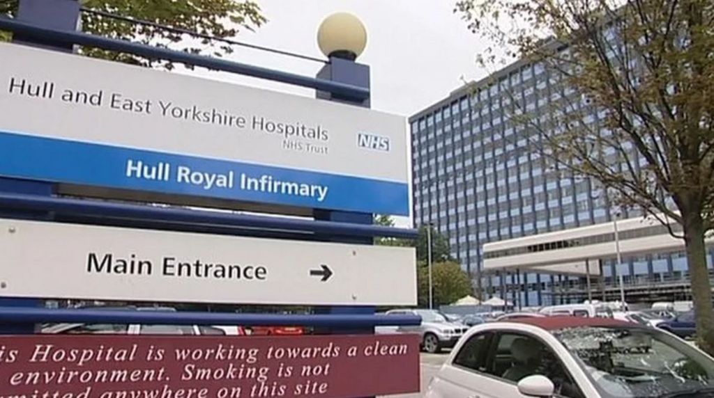 Sign at the entrance of Hull Royal Infirmary with cars and main multi-storey glass-fronted building in background