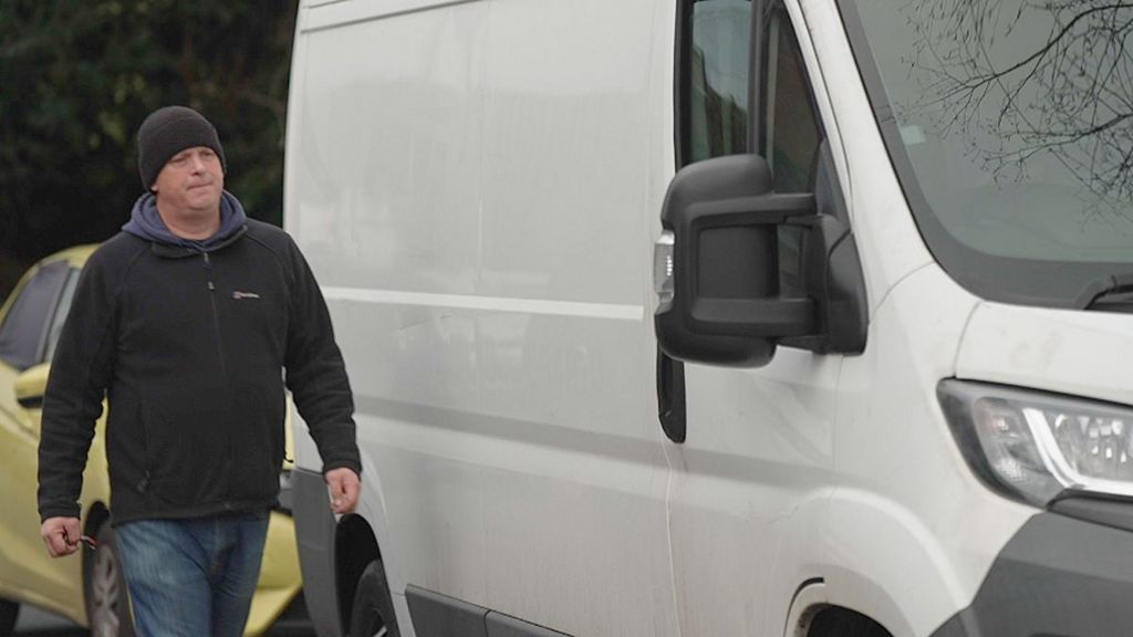 Dave wearing a black beanie and coat walks up to the door of his white van.