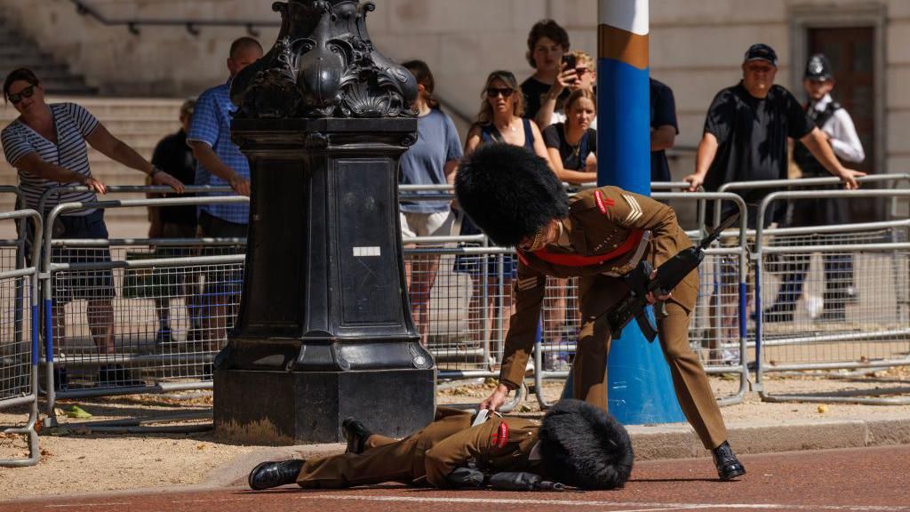 A foot guard is checked by another member of the Army after he fainted on the Mall