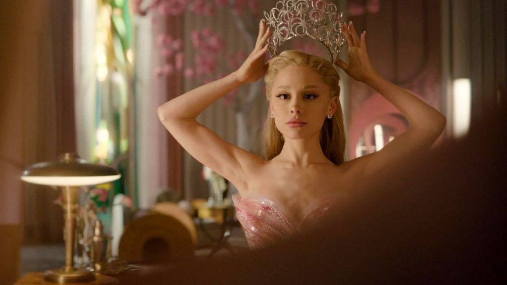 Ariana Grande in Wicked: For Good, as Glinda the good witch, wearing a pink dress and placing a tiara on her head